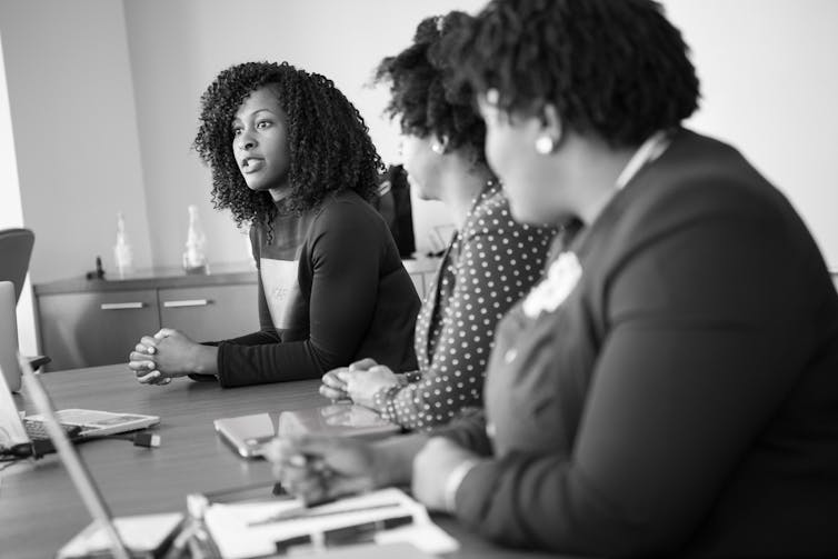 Three people of colour sit at a table, with one person speaking