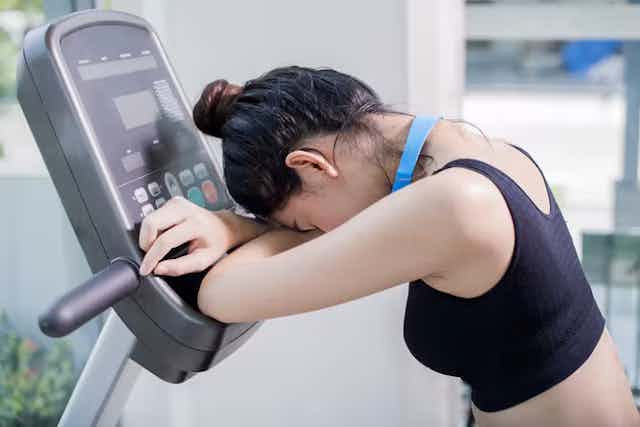 Wanita mengistirahatkan kepalanya di pegangan tangan treadmill