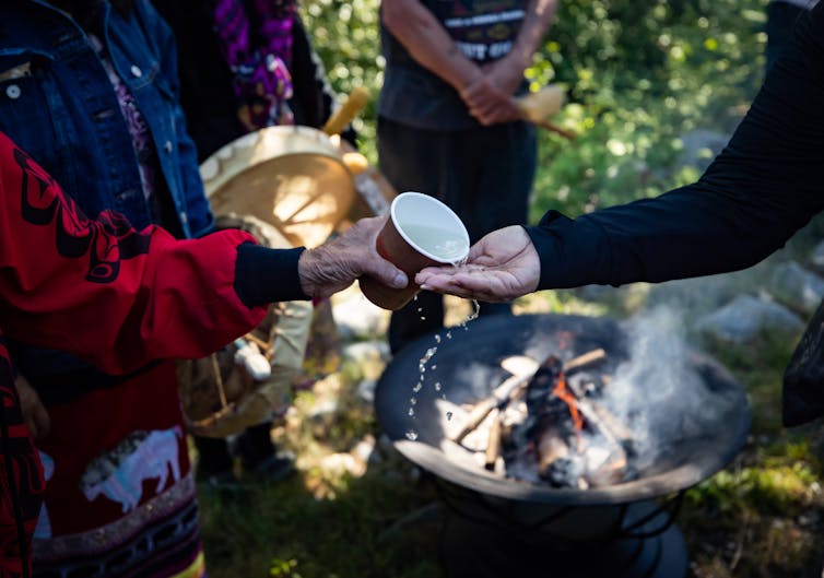 one person pours water from a cup into the hands of another