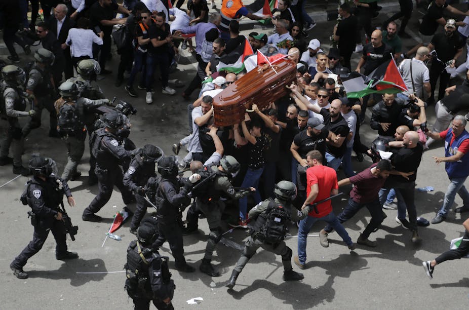 An aerial photo shoes police wielding batons hitting men carrying a coffin an waving Palestinian flags.