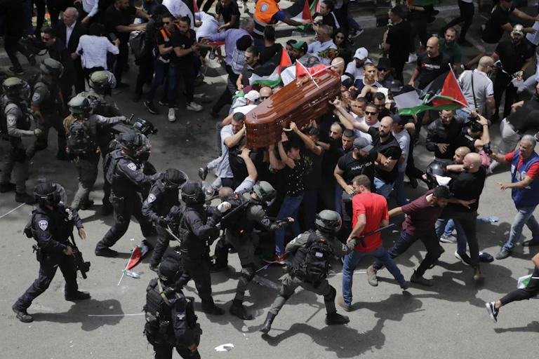An aerial photo shoes police wielding batons hitting men carrying a coffin an waving Palestinian flags.