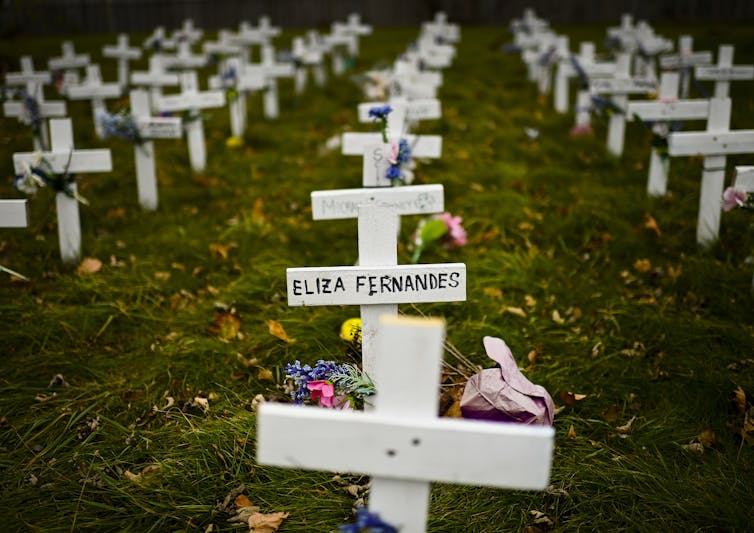 Small white crosses are displayed in a field with people's names written on them.