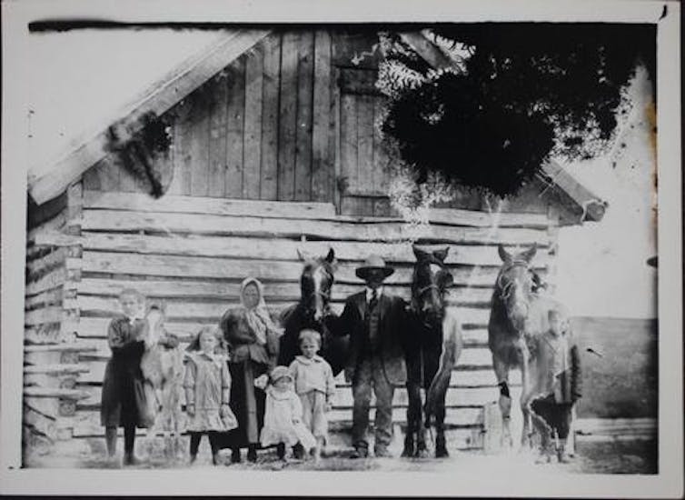 People seen in a black and white photo standing in front of a barn.