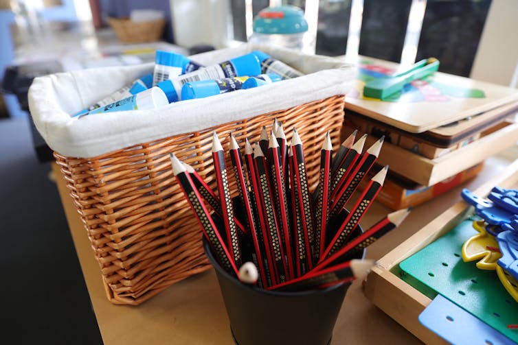 A bucket of glue sticks and sharpened pencils on a desk.