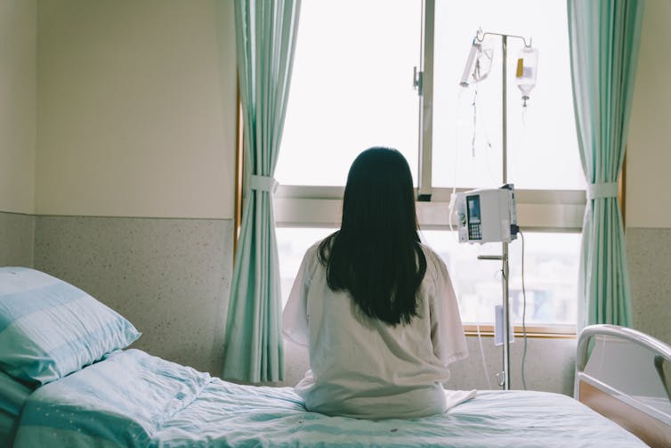 Woman sits on a hospital bed, her back to the door.
