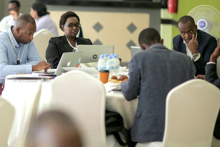 A group of formally dressed people sitting about a table and working on their laptops.