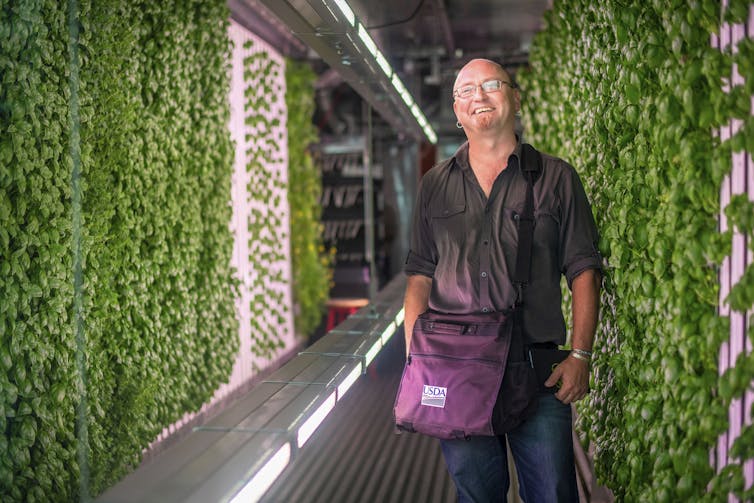 A person smiles against a background of vertical plants