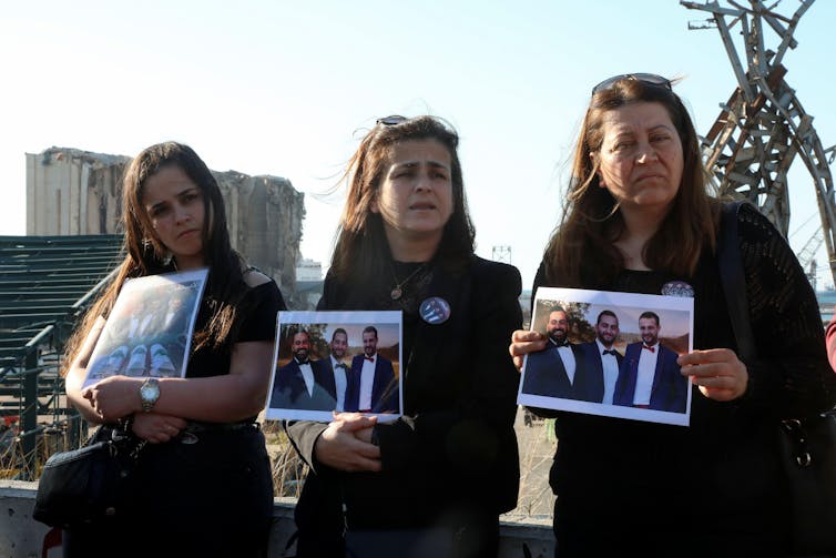 Three women carrying posters of the people who died in the Beirut blast.