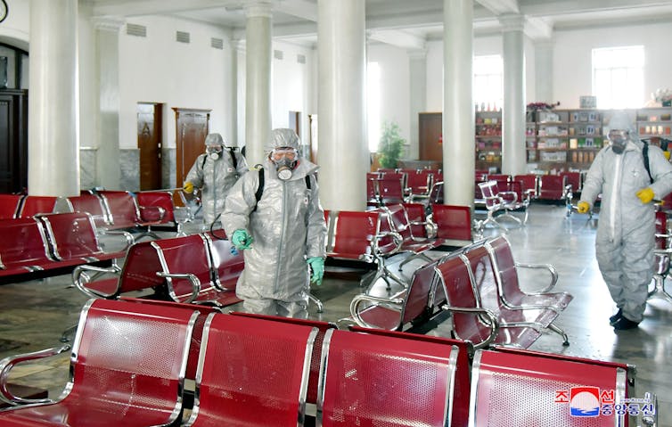 Workers dressed in full PPE deep cleaning a seating area.