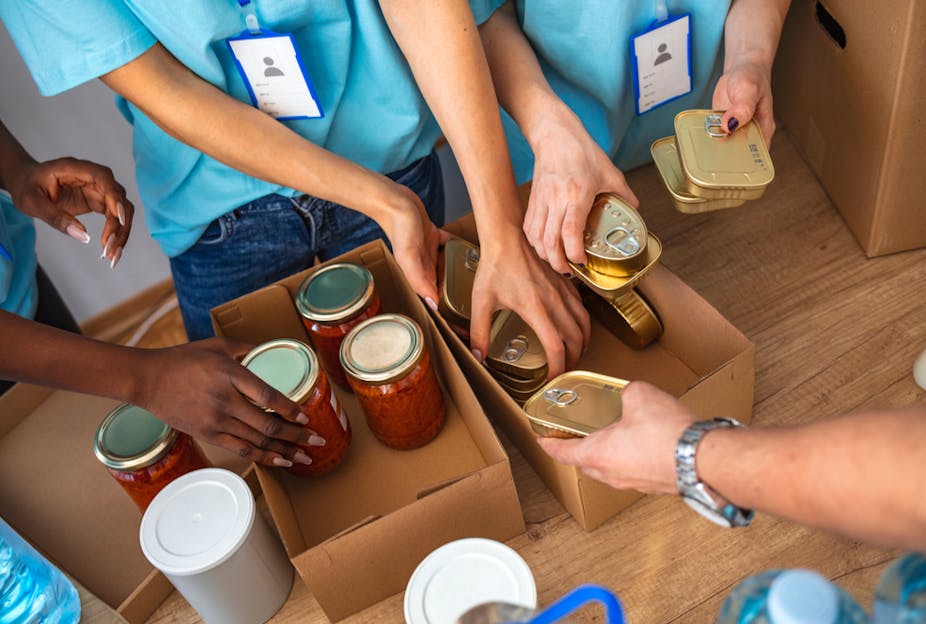 Hands of volunteers sorting jars of pasta sauce and tins of fish into carboard boxes