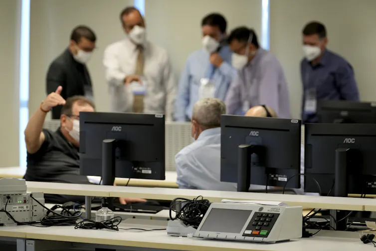 Men wearing masks bustle around computers