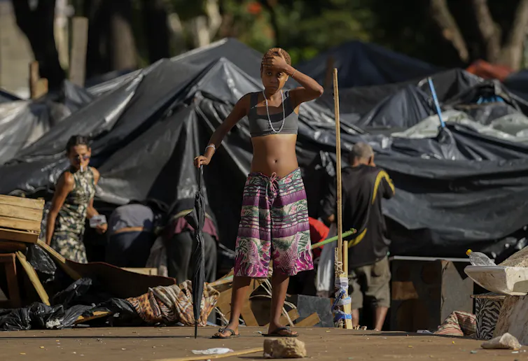 A woman stands in front of a temporary shelter, made of black tarps