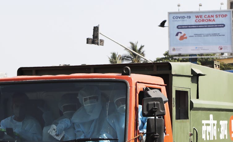 Men in masks sit in the cab of a garbage truck.