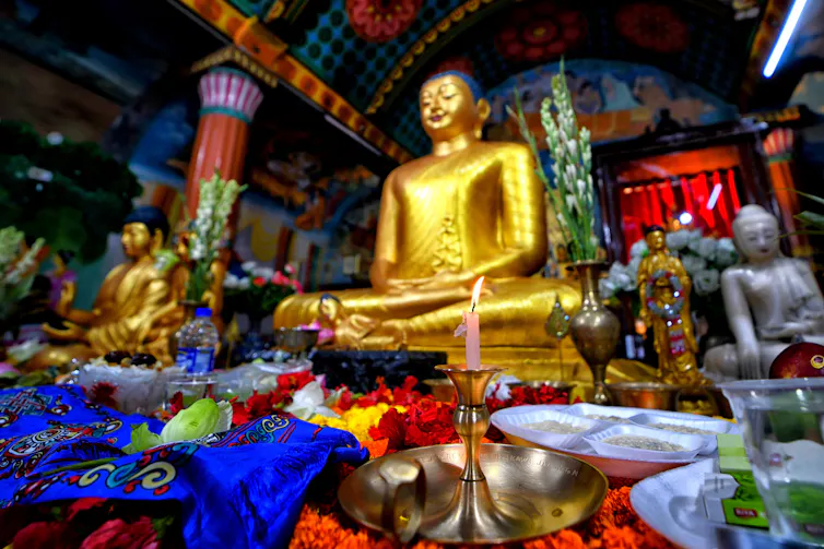 A large golden statue of the Buddha in a seated meditation pose inside a temple, with candles lit in front.
