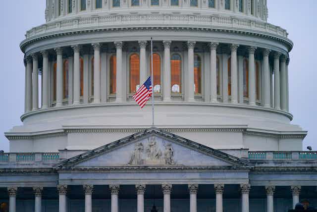 A US flag at half staff on a pole attached to the US Capitol building.