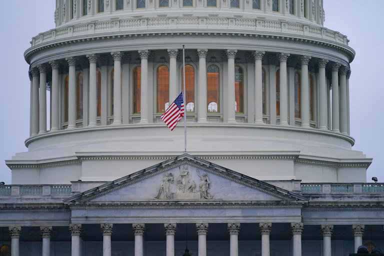 A US flag at half staff on a pole attached to the US Capitol building.