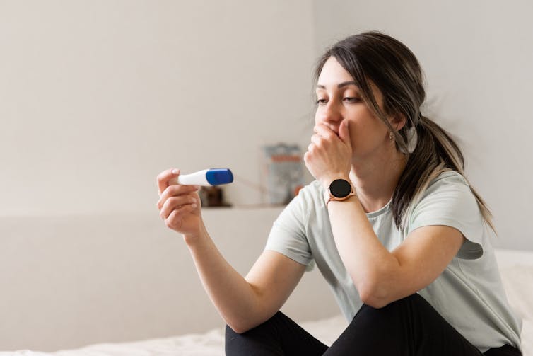 A woman looking at a pregnancy test with her hand over her mouth