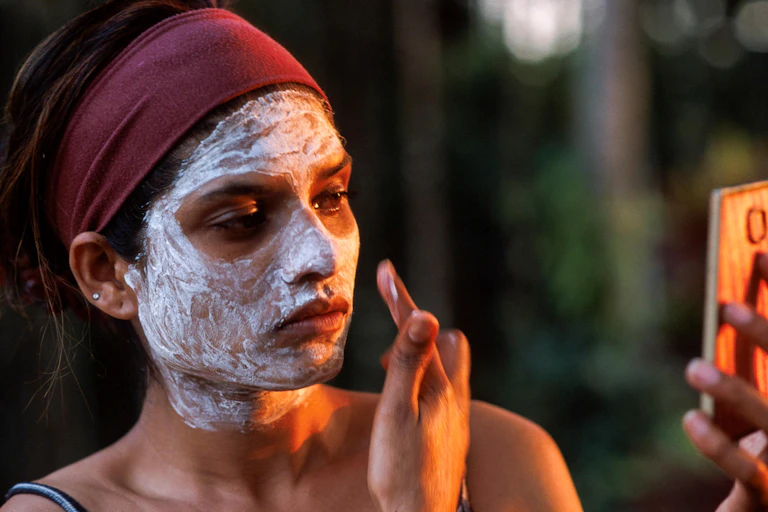 A woman applies white cream to her face.