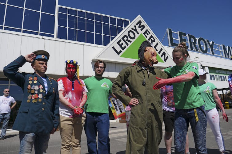 Protesters drenched in red paint standing outside a retail store.