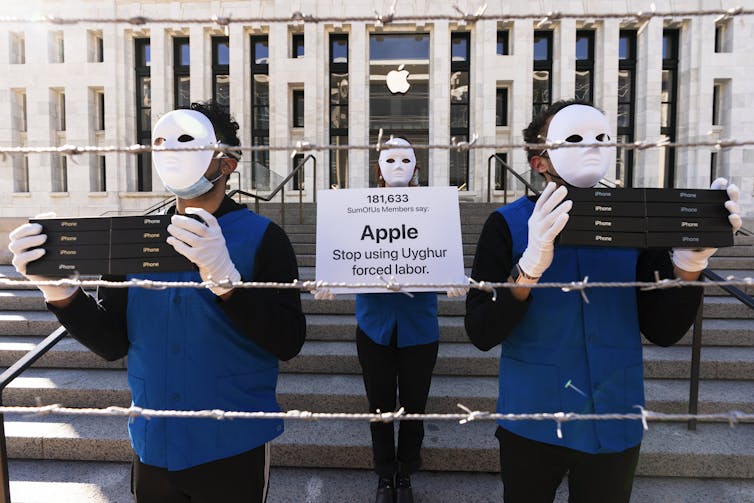 Protesters wearing masks and holding signs accusing Apple of using forced labour