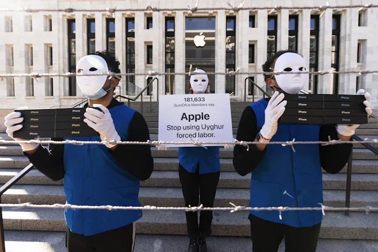 Protesters wearing masks and holding signs accusing Apple of using forced labour