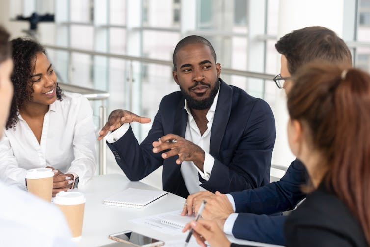 A man speaking to a group of people sitting around him at a table