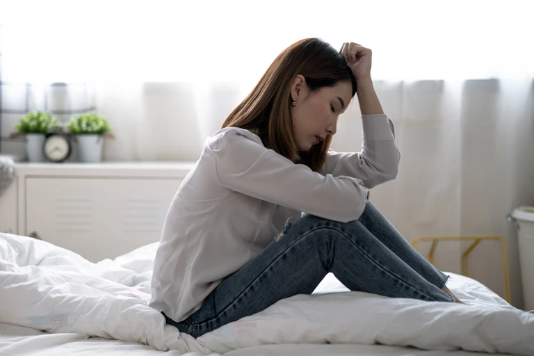 A young woman on a bed, appears despondent.