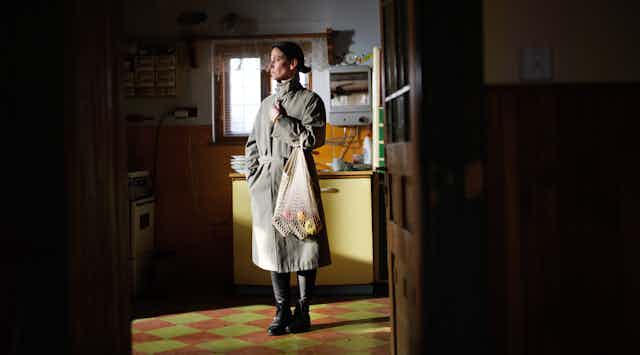 A woman stands alone in a simple kitchen.