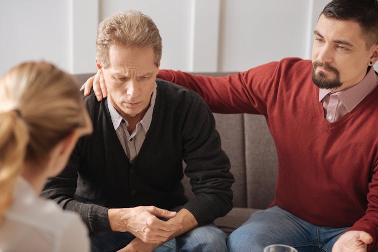 Man with hand on other man's shoulder sitting in front of female health worker