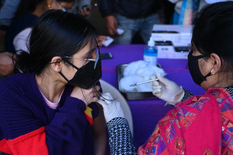 Vaccinator in India gives a COVID shot.