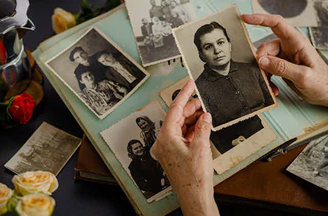 A person's hands holding a black and white photograph against a scrapbook of photos