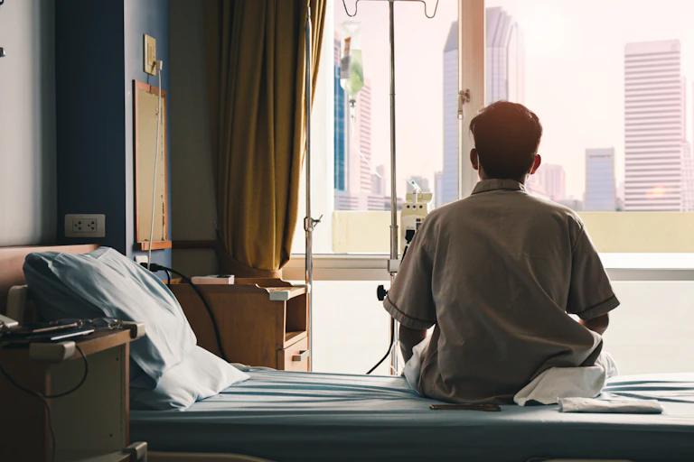 A patient looks out a window while sitting on a bed.