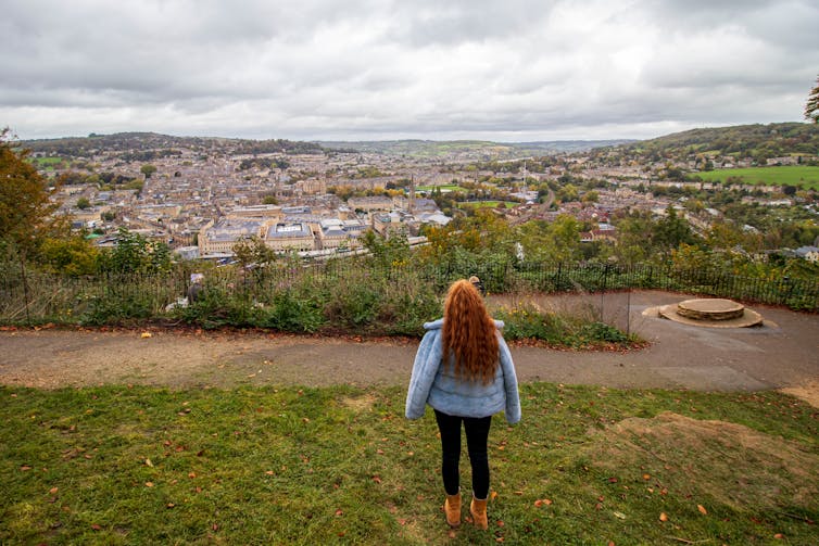 Person stands on grassy hill and looks over town