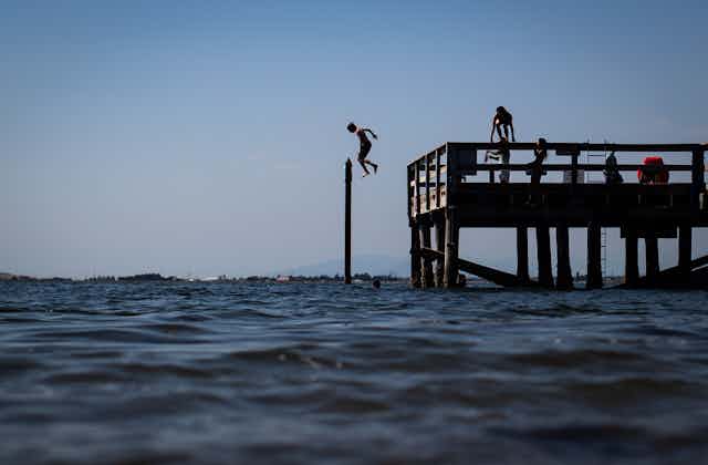 A boy jumps off a pier into the water