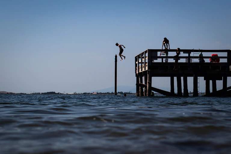 A boy jumps off a pier into the water