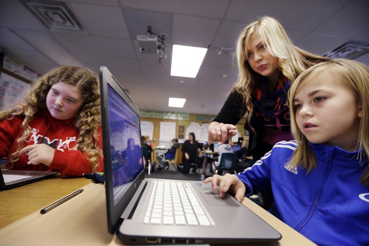 Girls work on computers while a woman assists.