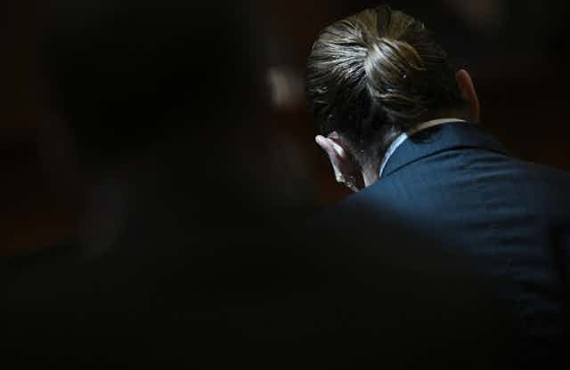 Johnny Depp's pony-tailed hair is seen in a dimly lit courtroom.