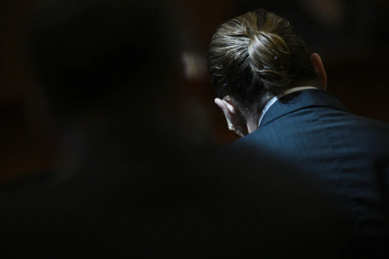 Johnny Depp's pony-tailed hair is seen in a dimly lit courtroom.