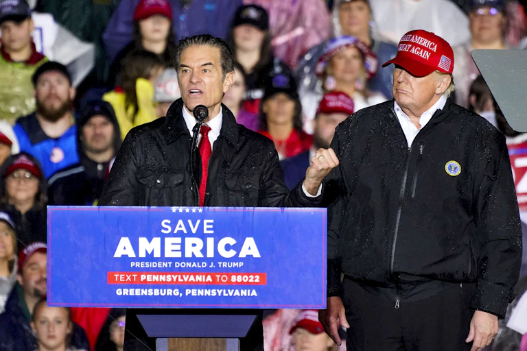 Donald Trump wearing a red 'Make America Great Again' hat looks on as Senate candidate Mehmet Oz speaks at a platform.