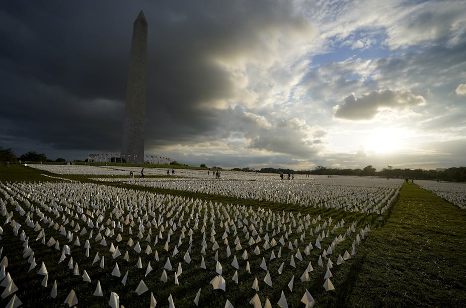 A tall monument stands amid a field of many small white flags stuck in the ground.
