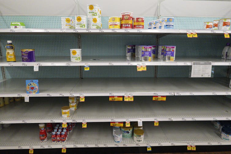 Shelves at a a grocery store are mostly bare with a small number of baby formula packages here and there