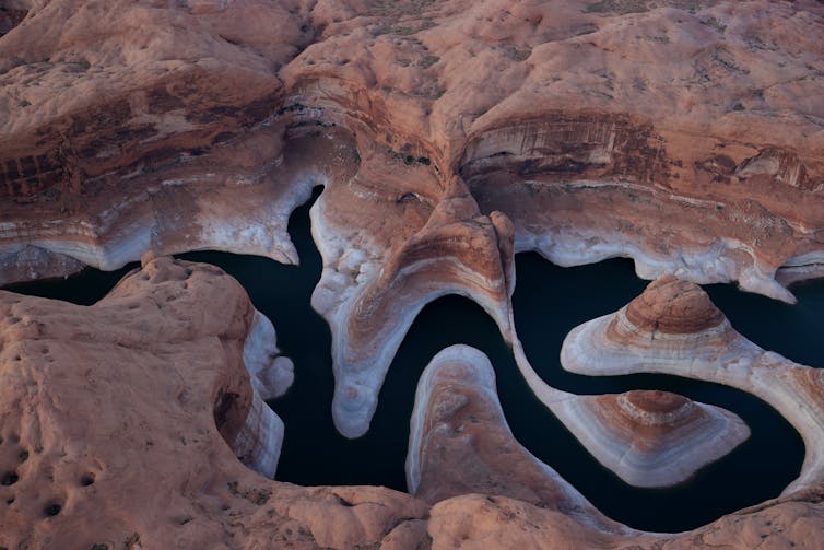 Viewed from an airplane, a long lake snakes through a canyon with a wide white rim around its edge.