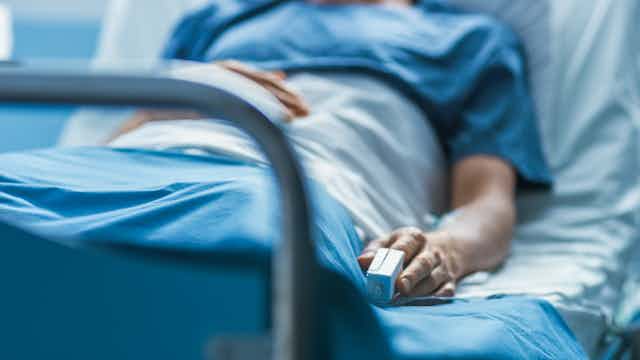 Person lying in hospital bed with monitor clipped to finger