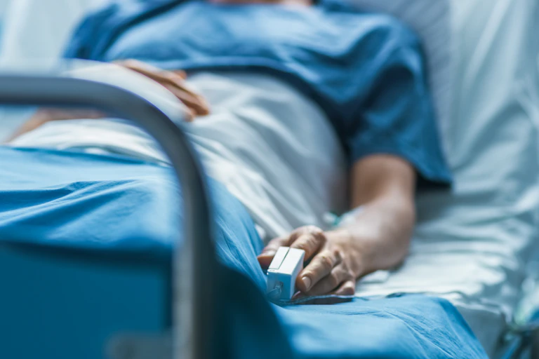 Person lying in hospital bed with monitor clipped to finger