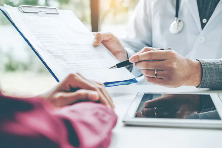 Doctor pointing pen to clipboard while patient waits