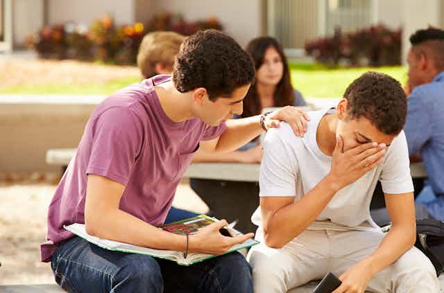 A male student comforts a distressed classmate