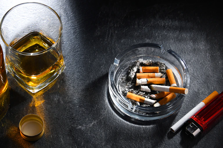 Un cendrier remplit de mégots est posé à côté d'un verre d'alcool