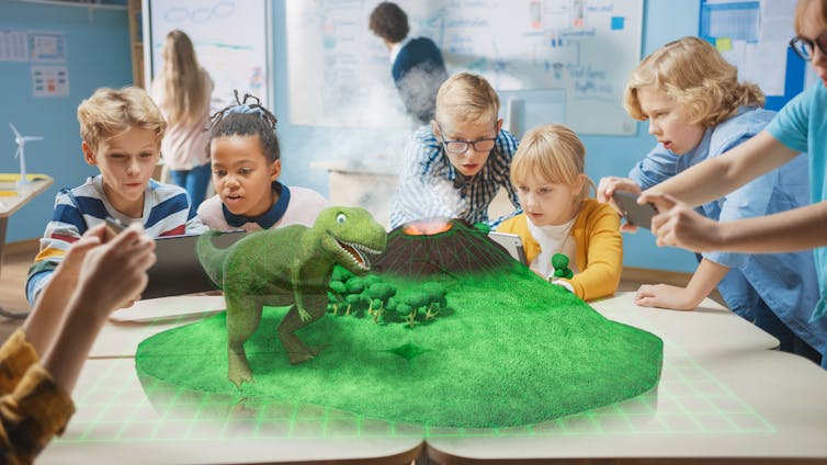 children using laptops sit at a table with a digital dinosaur hologram in the middle