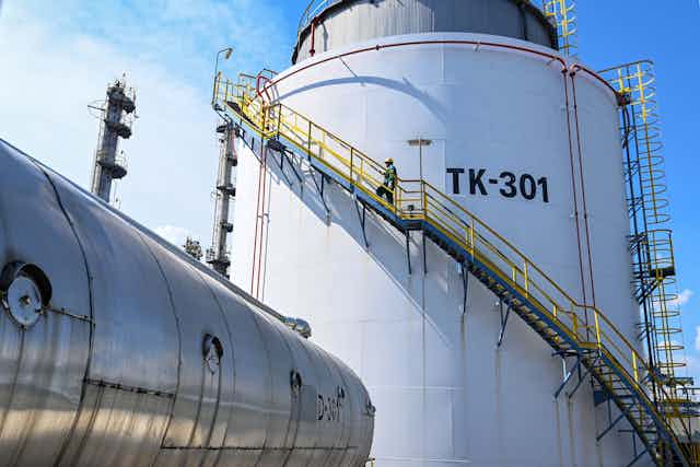 A worker climbs an external staircase around a large storage tank