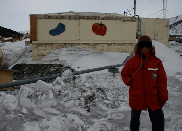 A person standing in front of a building in the snow with a pepper and tomato painted on the side.